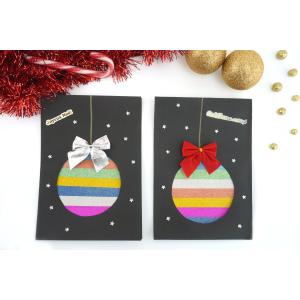 Découvrez comment réaliser une jolie carte de vœux boule de Noël ! Avec du masking tape, un nœud en tissu, des strass étoiles et des gommettes, nous allons réaliser une sublime carte de Noël que les e